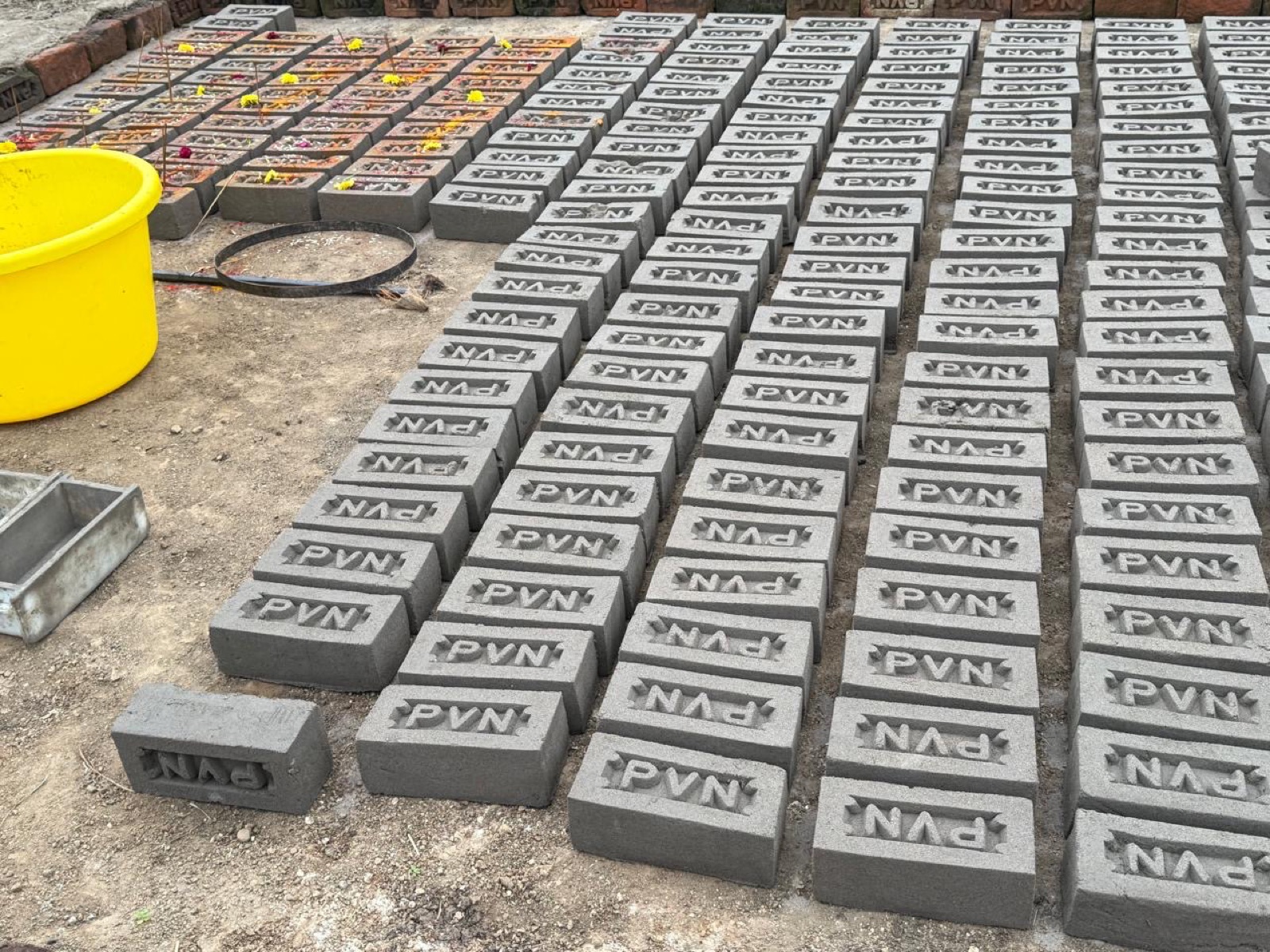 Grey raw bricks stamped PVN laid out beside a steel mould